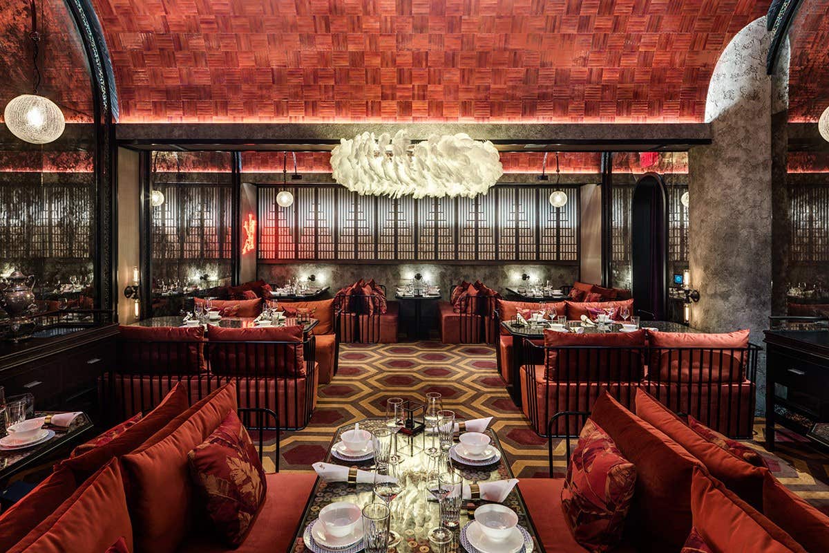 Luxurious restaurant with red velvet seating, ornate lighting, and an opulent ceiling. Tables are set for dining.