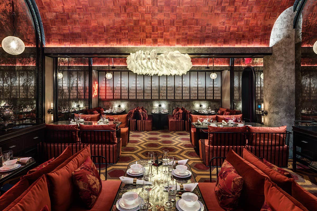 Luxurious restaurant with red velvet seating, ornate lighting, and an opulent ceiling. Tables are set for dining.