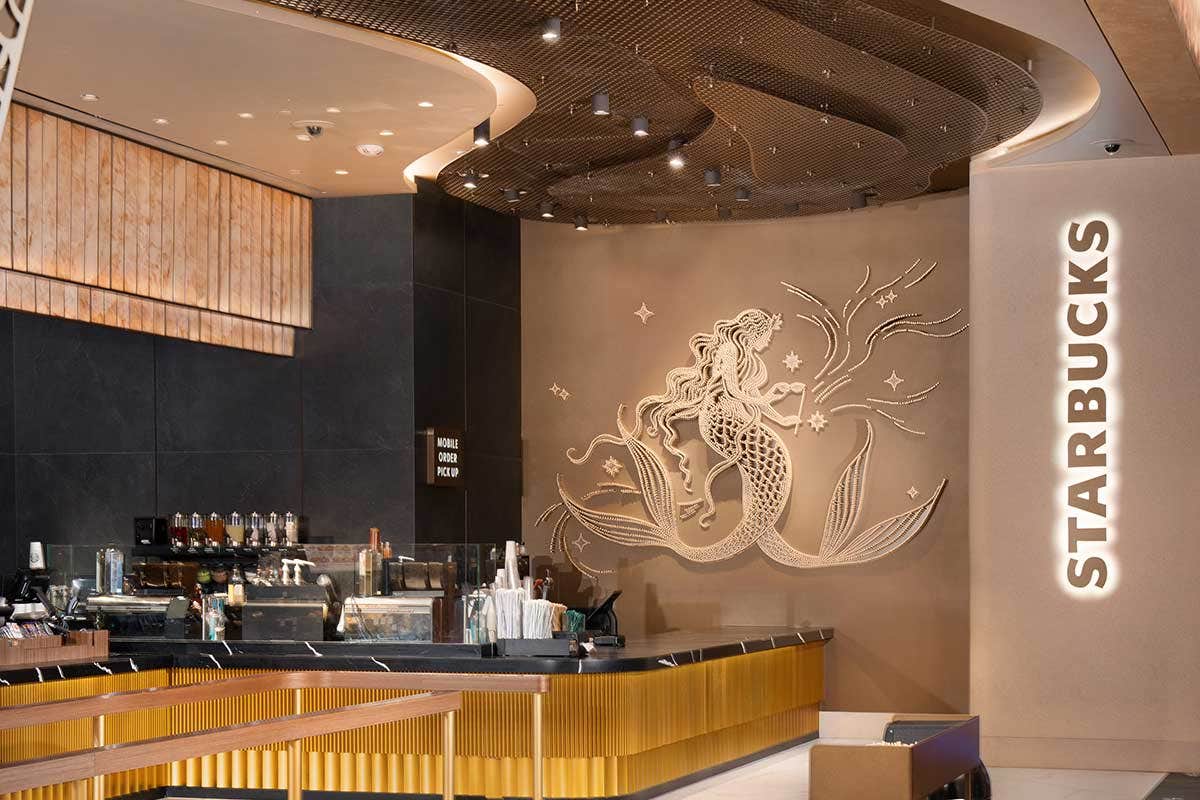 A modern Starbucks interior with a decorative wall featuring a mermaid artwork, and baristas working behind the counter.