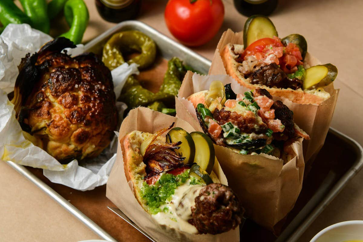 Three stuffed pita breads with meat, pickles, and vegetables, served on a tray with roasted cauliflower and green peppers.