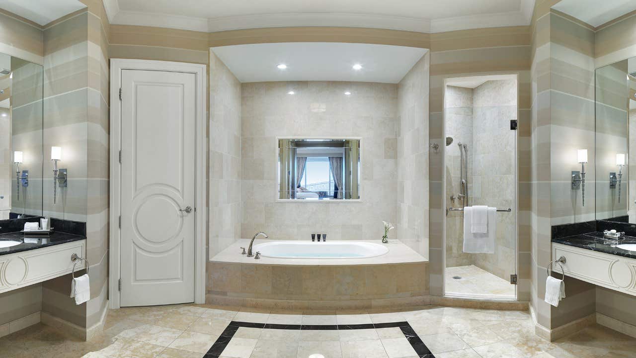 Elegant bathroom with a central bathtub, walk-in shower, dual sinks with mirrors, and neutral-toned tiles and walls.