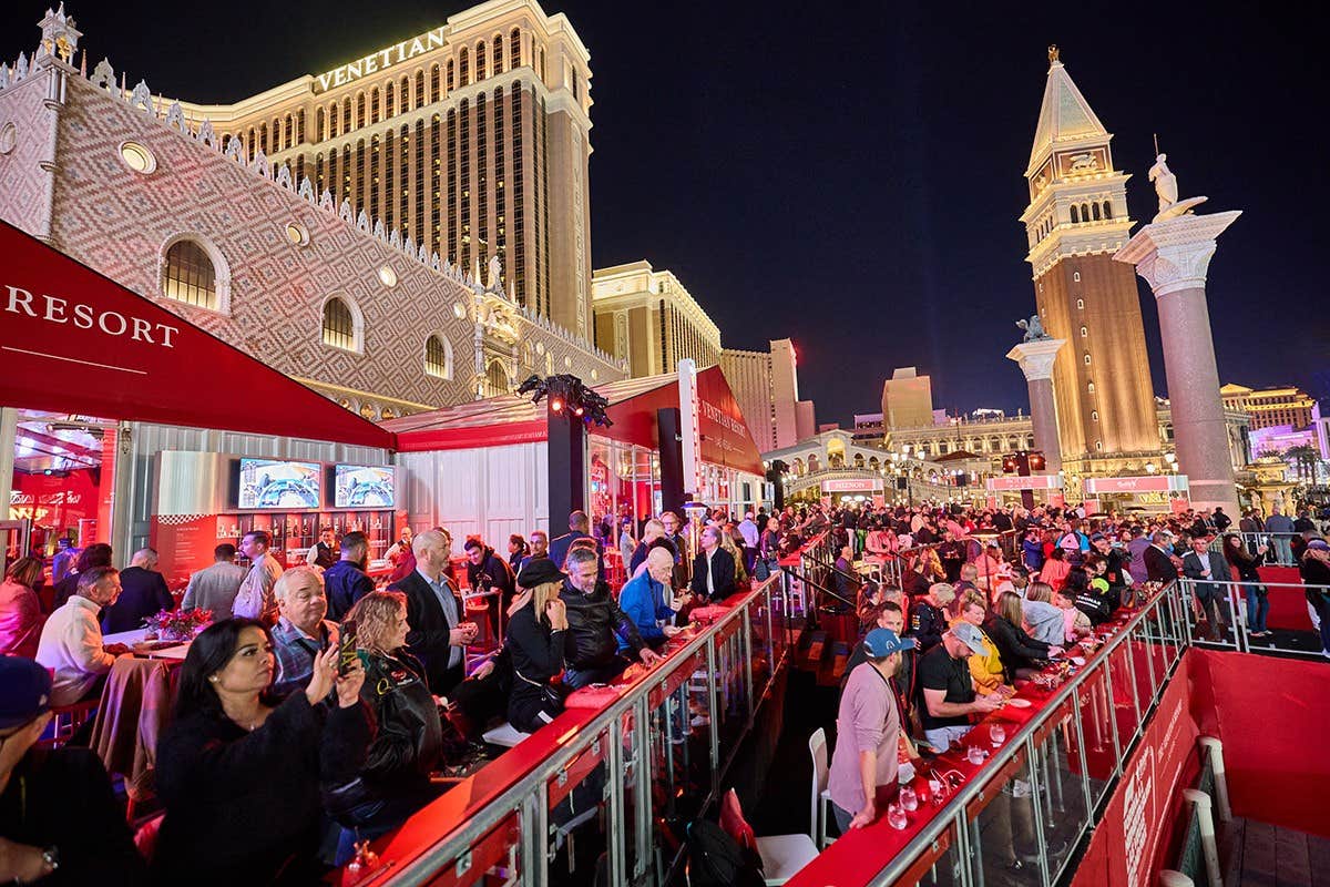 Crowd enjoying an outdoor event with Venetian Resort and replica St. Mark's Campanile lit up in the background at night.