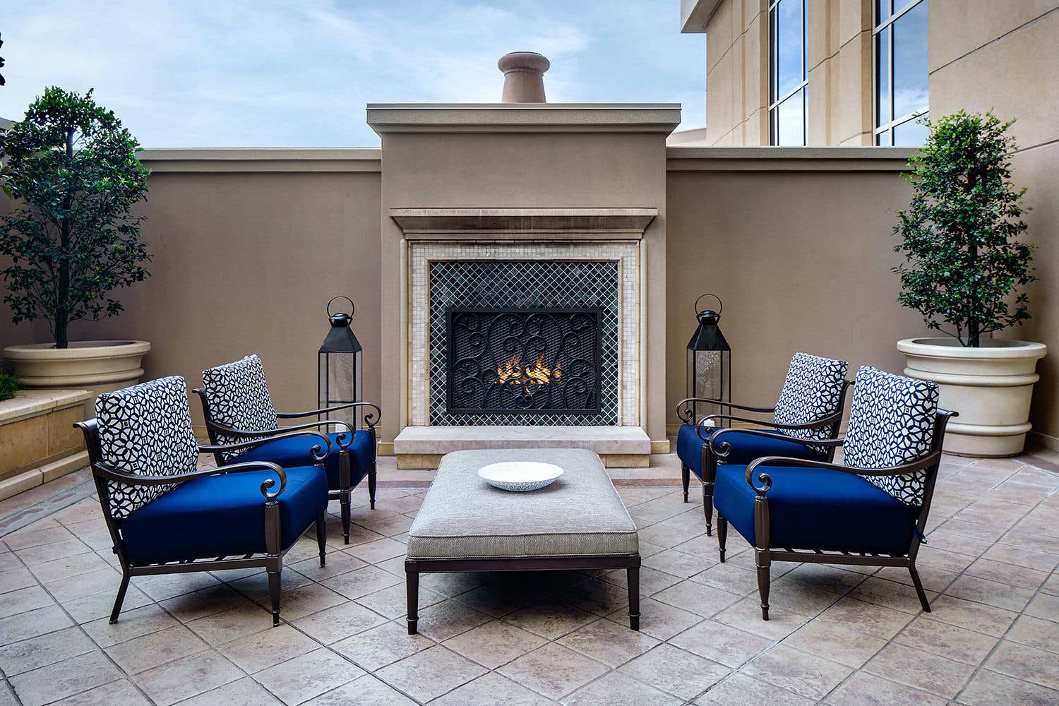 The outdoor patio space af a parlor with 4 chairs, a coffee table, and a fireplace.