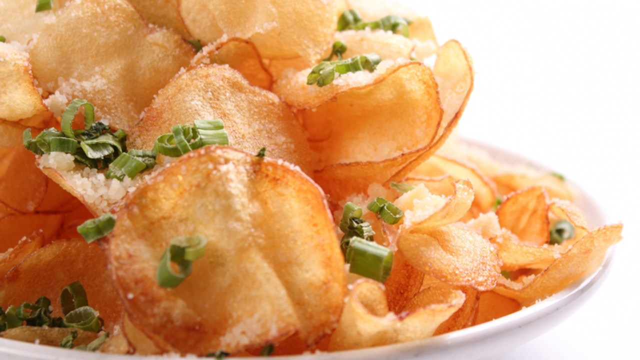 A bowl filled with crispy potato chips topped with green onions and grated cheese.