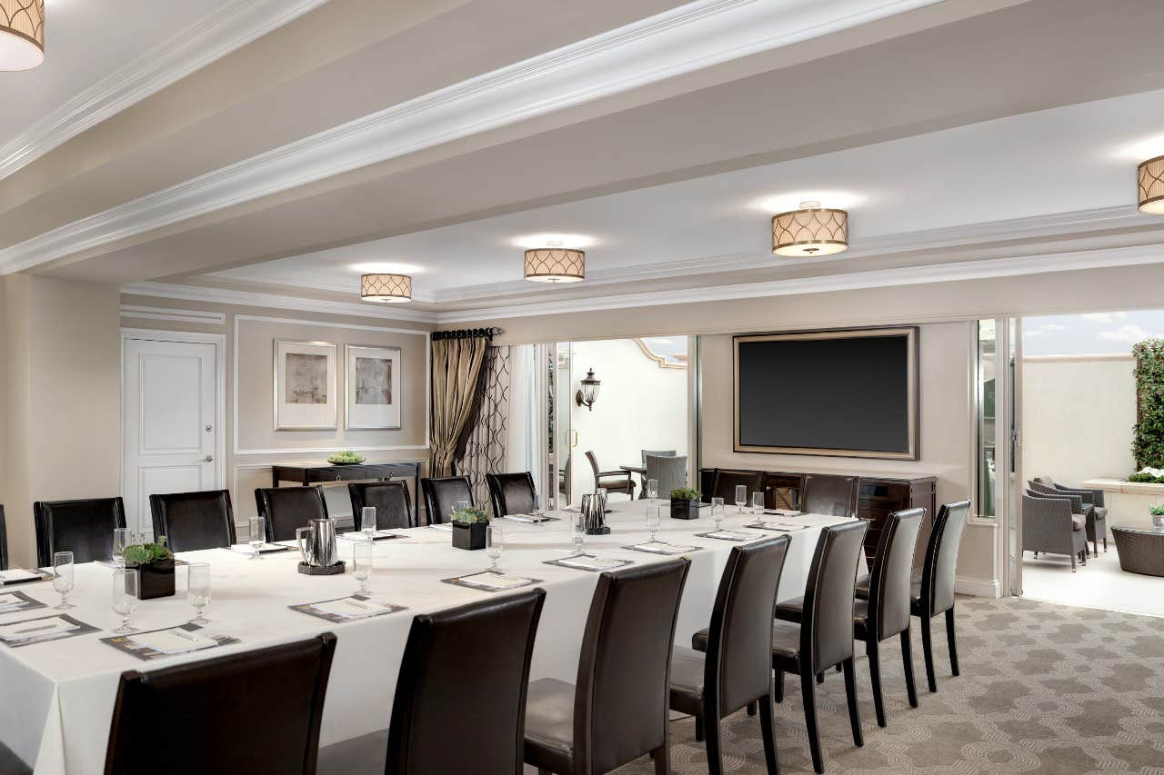 Elegantly set conference room with a long table, chairs, a blank screen, and minimalistic décor.