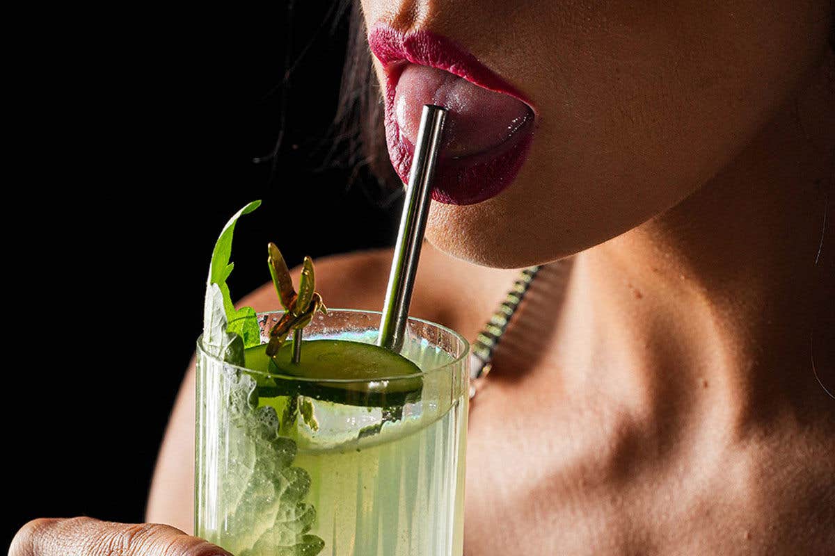 Close-up of a person drinking from a glass with a metal straw, featuring a garnish.