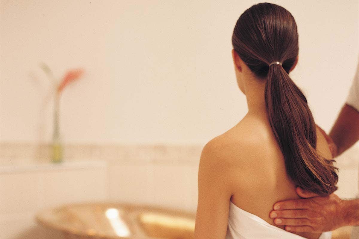 A person with long hair receives a shoulder massage in a serene, softly lit setting.