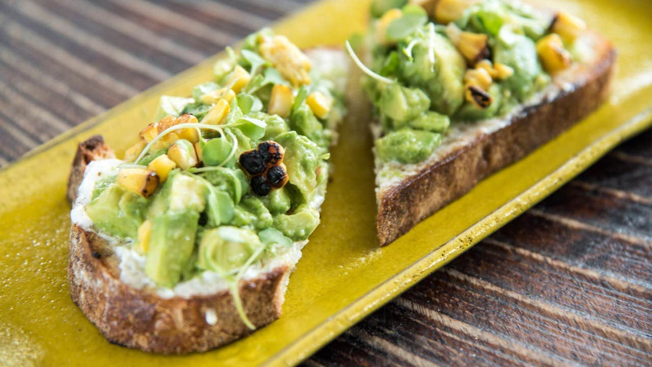 Two slices of avocado toast topped with grilled corn and greens on a yellow plate.