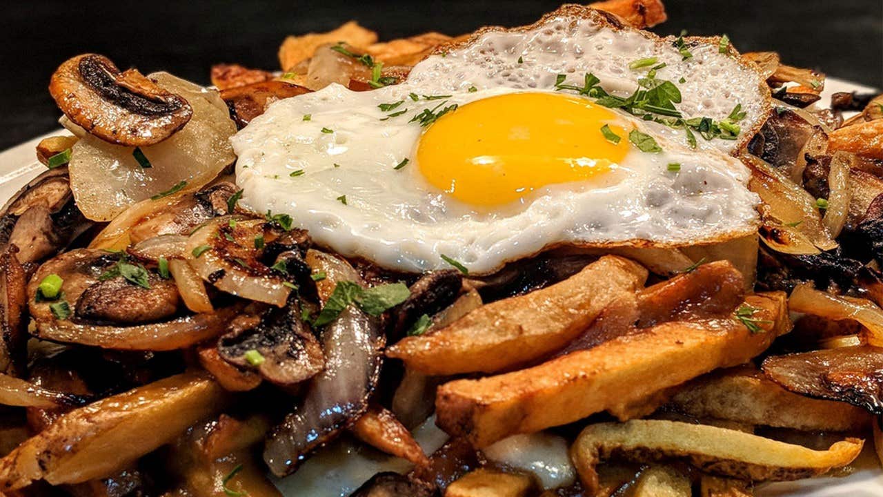 A plate of fries topped with sautéed mushrooms, onions, and a sunny-side-up egg, garnished with herbs.