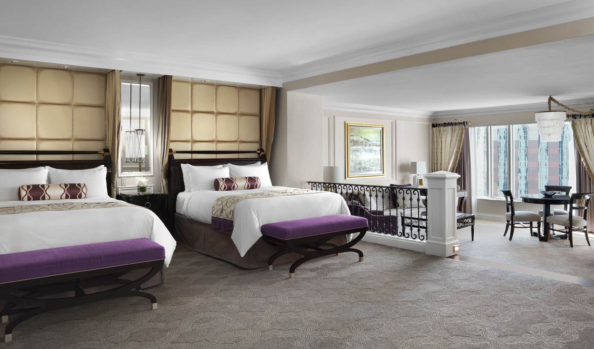 Luxurious hotel room with two double beds, purple benches, elegant decor, carpeted floor, and separate seating area.