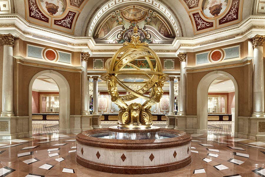 Ornate indoor fountain with a golden globe sculpture, surrounded by arched doorways and intricate ceiling artwork.