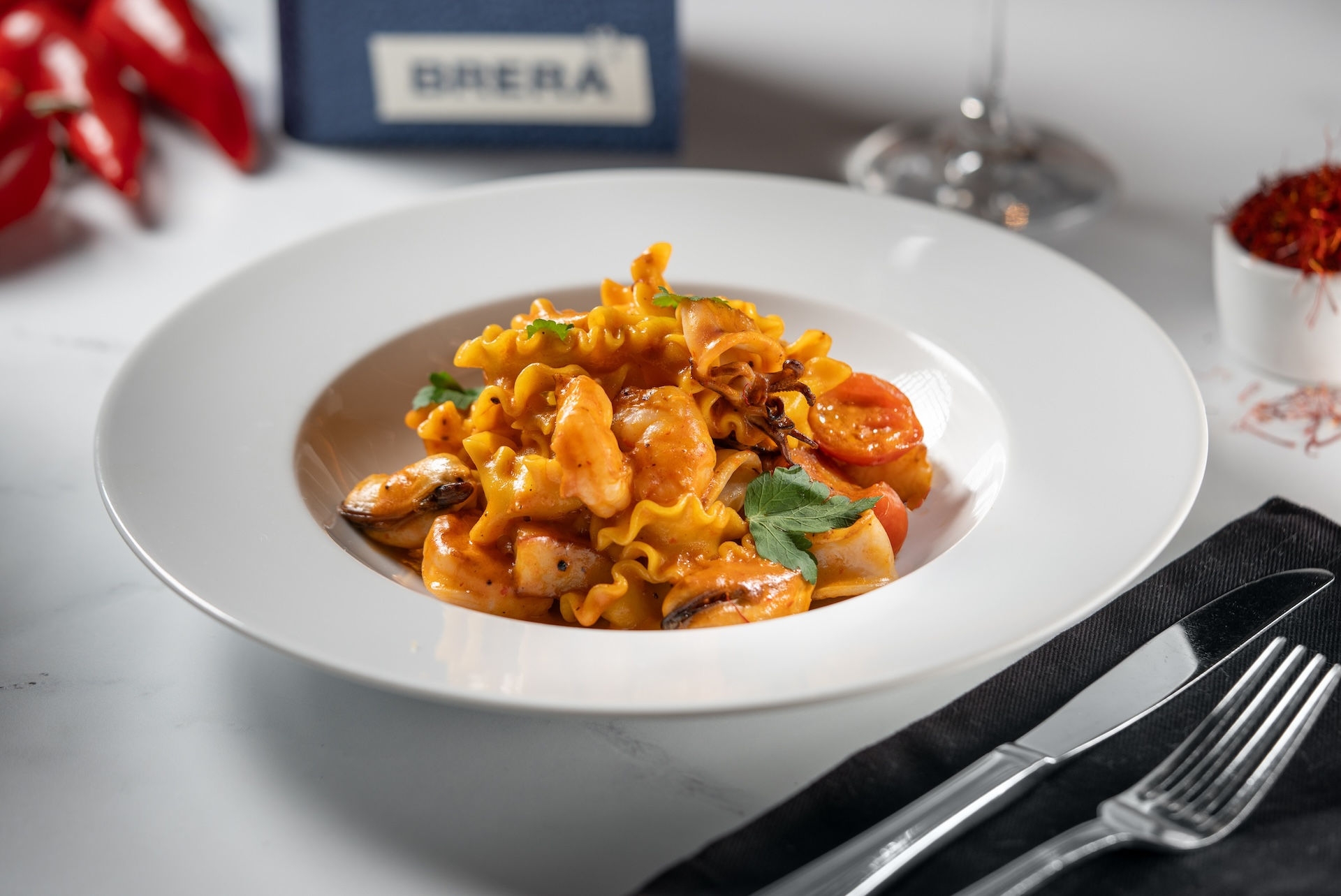 A seafood pasta dish in a red sauce with thick pasta, tomatoes, shrimp and basil.