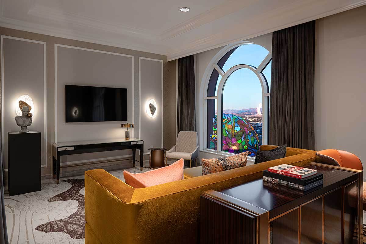 A modern living room with a mustard yellow sofa, flat-screen TV, arched window, and city view.