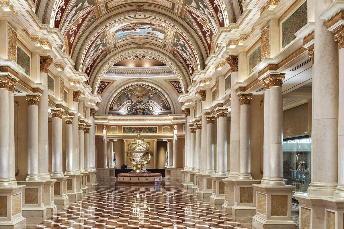 Ornate hallway with marble columns, frescoed ceilings, intricate moldings, and a gold armillary sphere at the center.