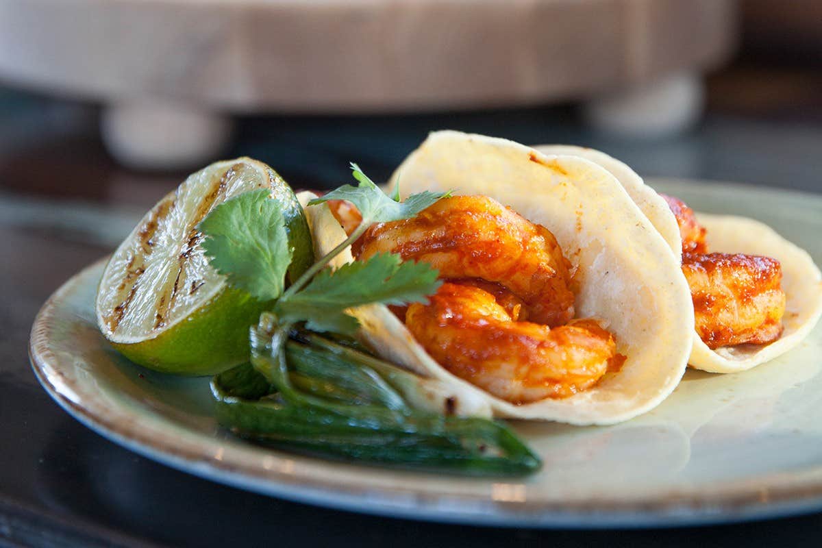 Shrimp tacos garnished with cilantro, grilled lime, and green chili on a light green plate.