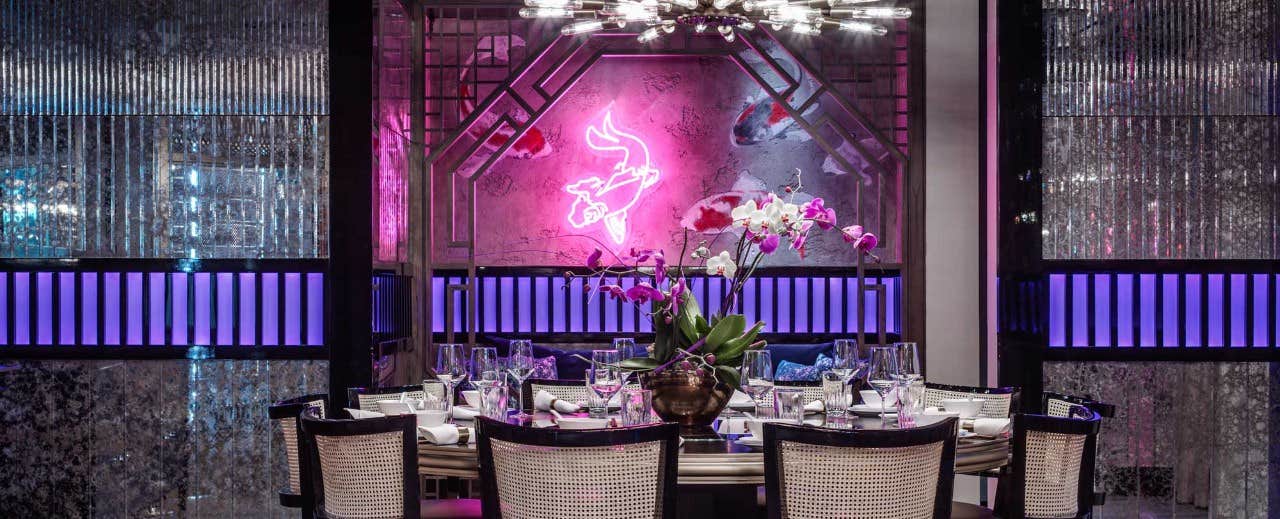 Elegant dining room with neon artwork, purple lighting, and a set table with flowers as centerpiece.