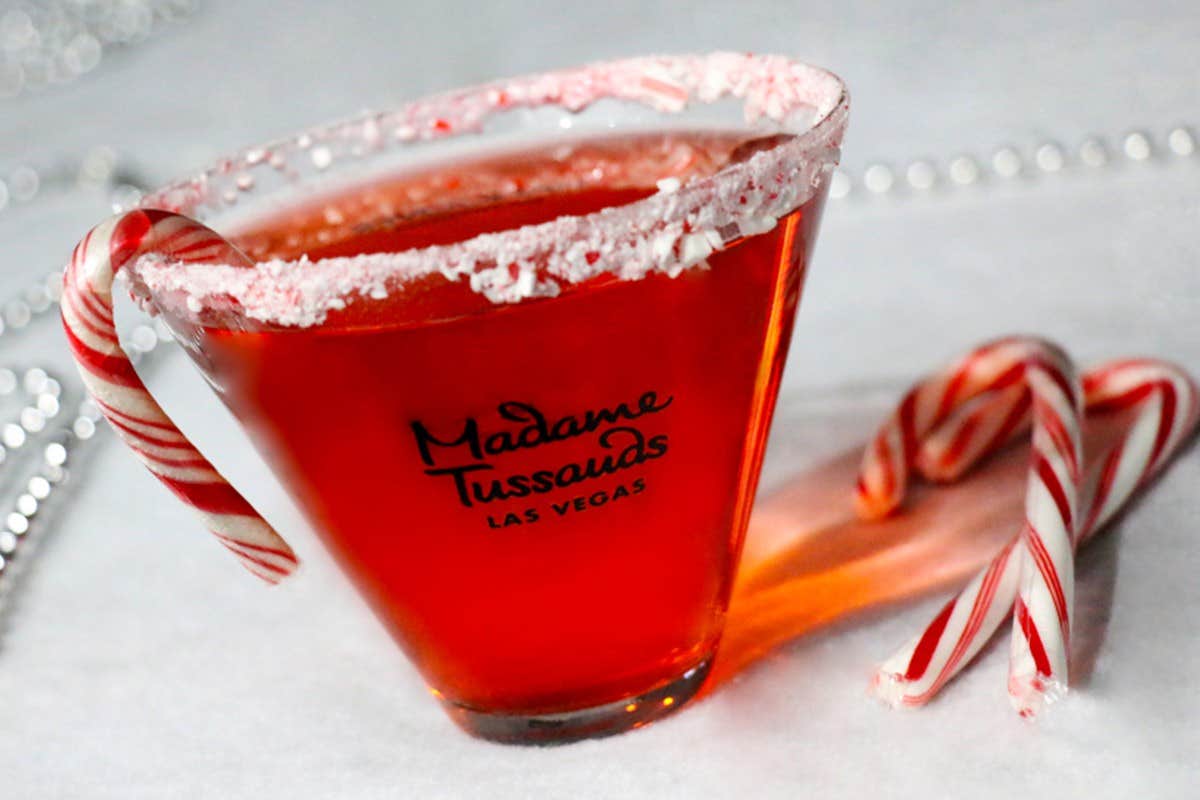 Red cocktail in a glass rimmed with crushed candy canes, labeled "Madame Tussauds Las Vegas," with candy canes beside it.