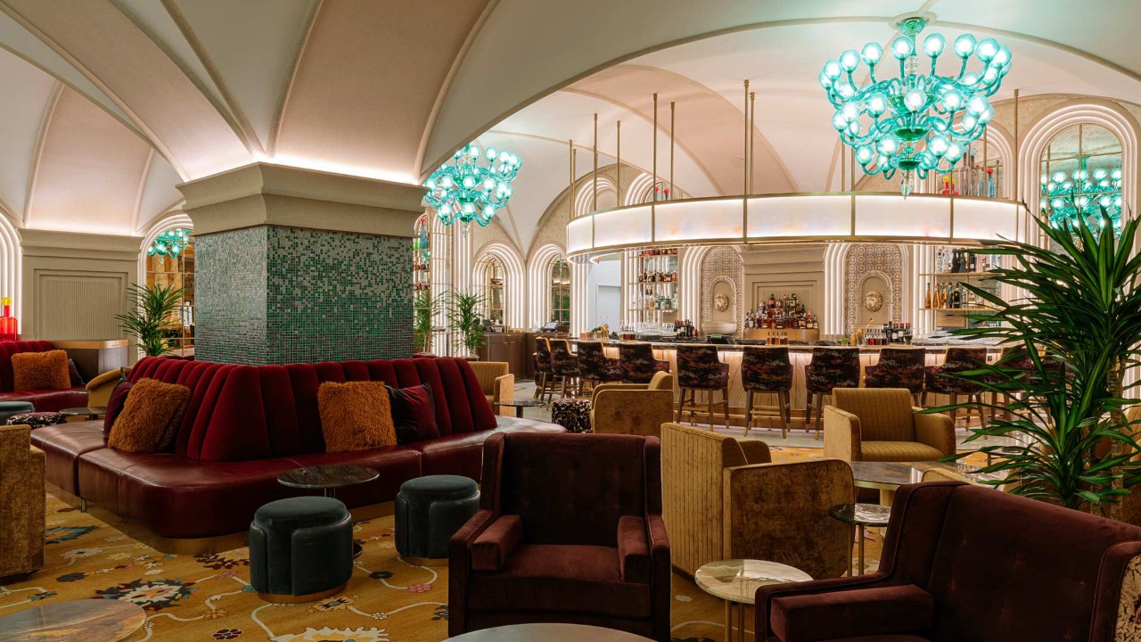 Luxurious lounge with modern decor, plush seating, green chandeliers, and a stylish bar under an arched ceiling.