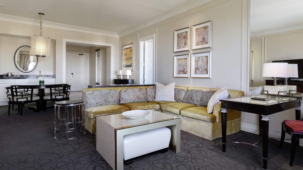 Modern living room with a sectional sofa, a coffee table, wall art, and a dining area with a round mirror and pendant light.