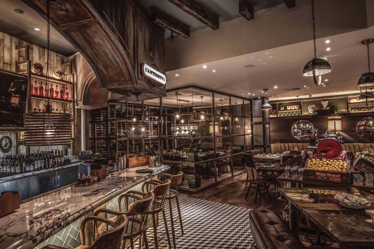 A stylish restaurant interior with a marble bar, wooden chairs, hanging lights, and a cozy dining area.