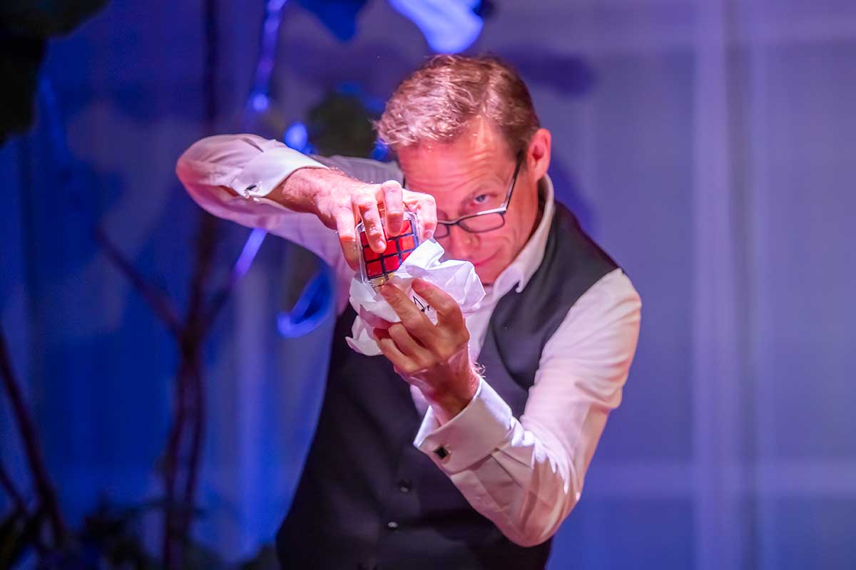 Man in a vest holding a Rubik’s Cube and crumpled paper.