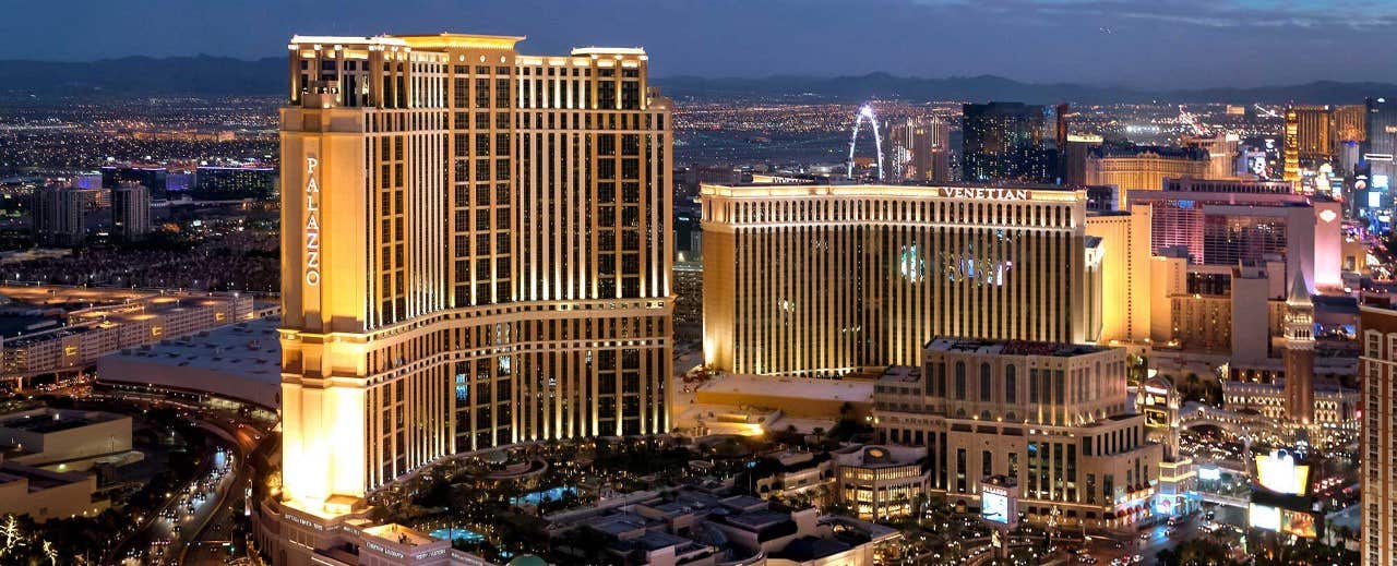 Las Vegas Strip at night, featuring illuminated hotels and casinos against a backdrop of city lights and mountains.