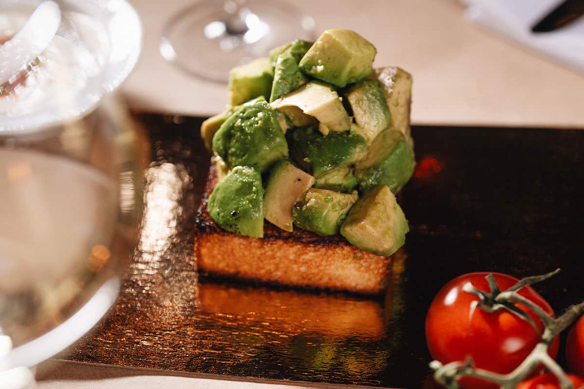 A piece of toast with chunks of avocados on the top on a dark-colored plate. 