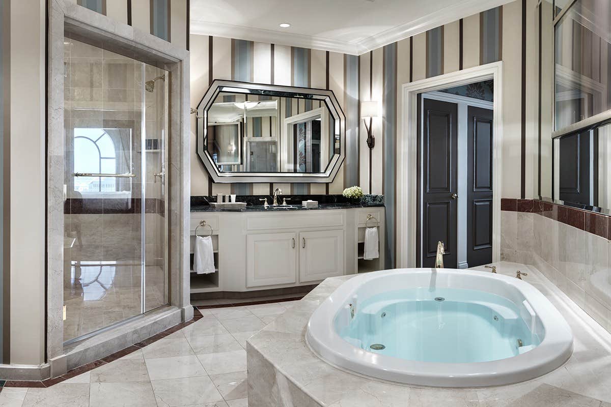 A luxurious bathroom with a soaking tub, glass-enclosed shower, large mirror, double sink vanity, and striped walls.