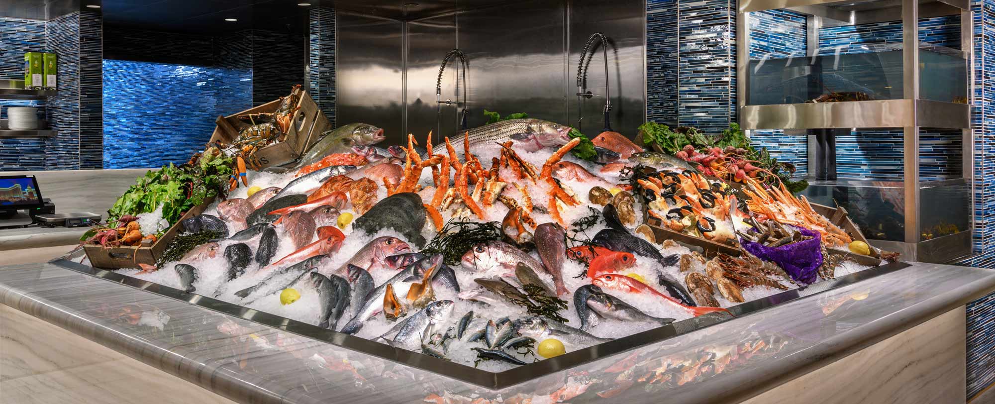 A seafood display on ice with various fish, shellfish, and crustaceans, surrounded by garnishes, in a modern setting.