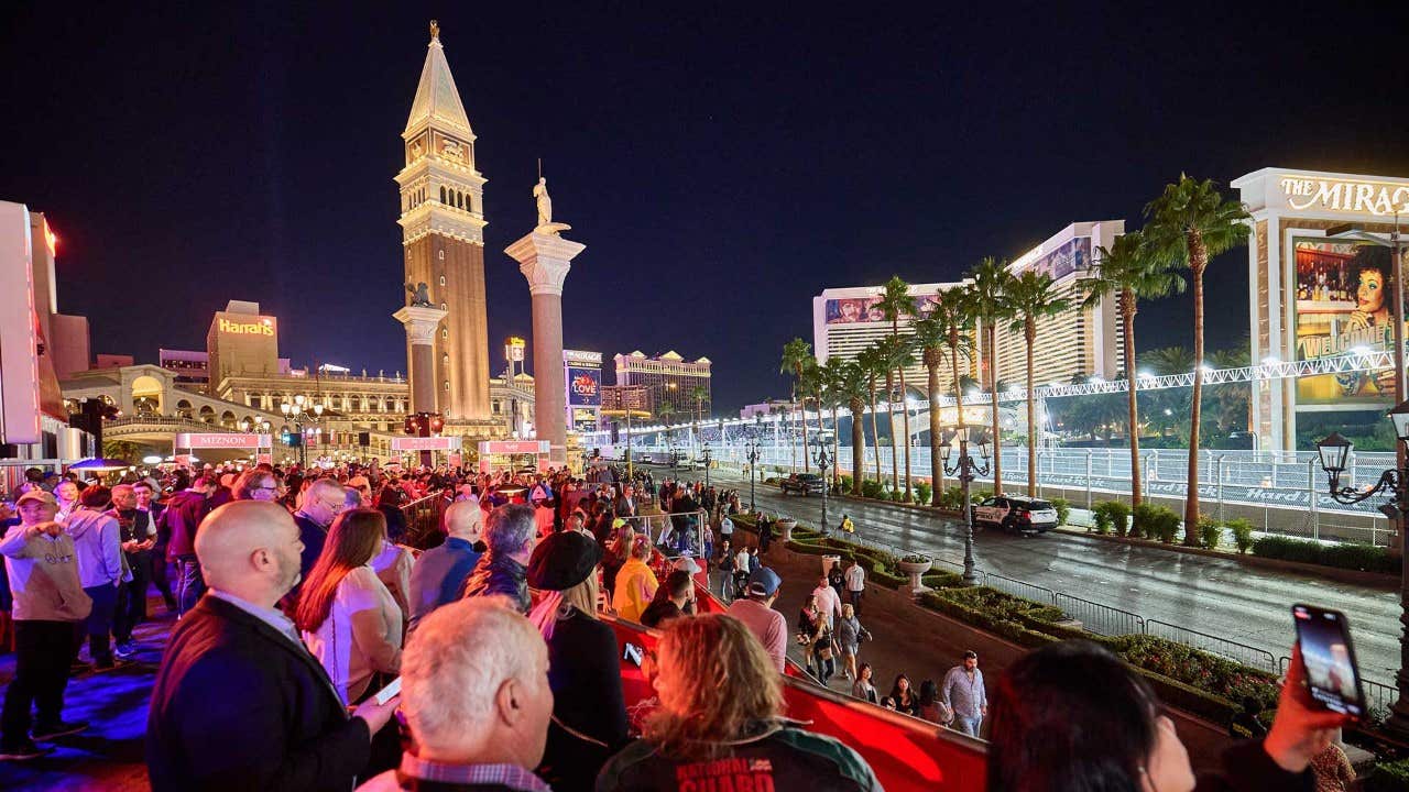 Crowd watches a night event on the Las Vegas Strip, featuring illuminated buildings and the iconic Venetian tower.