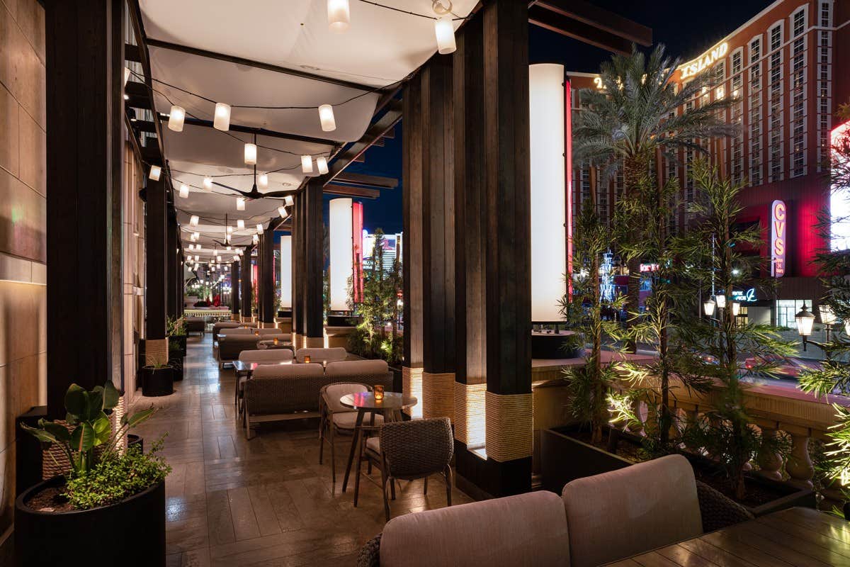 Outdoor restaurant seating area at night with modern decor, ambient lighting, plants, and a busy street in the background.