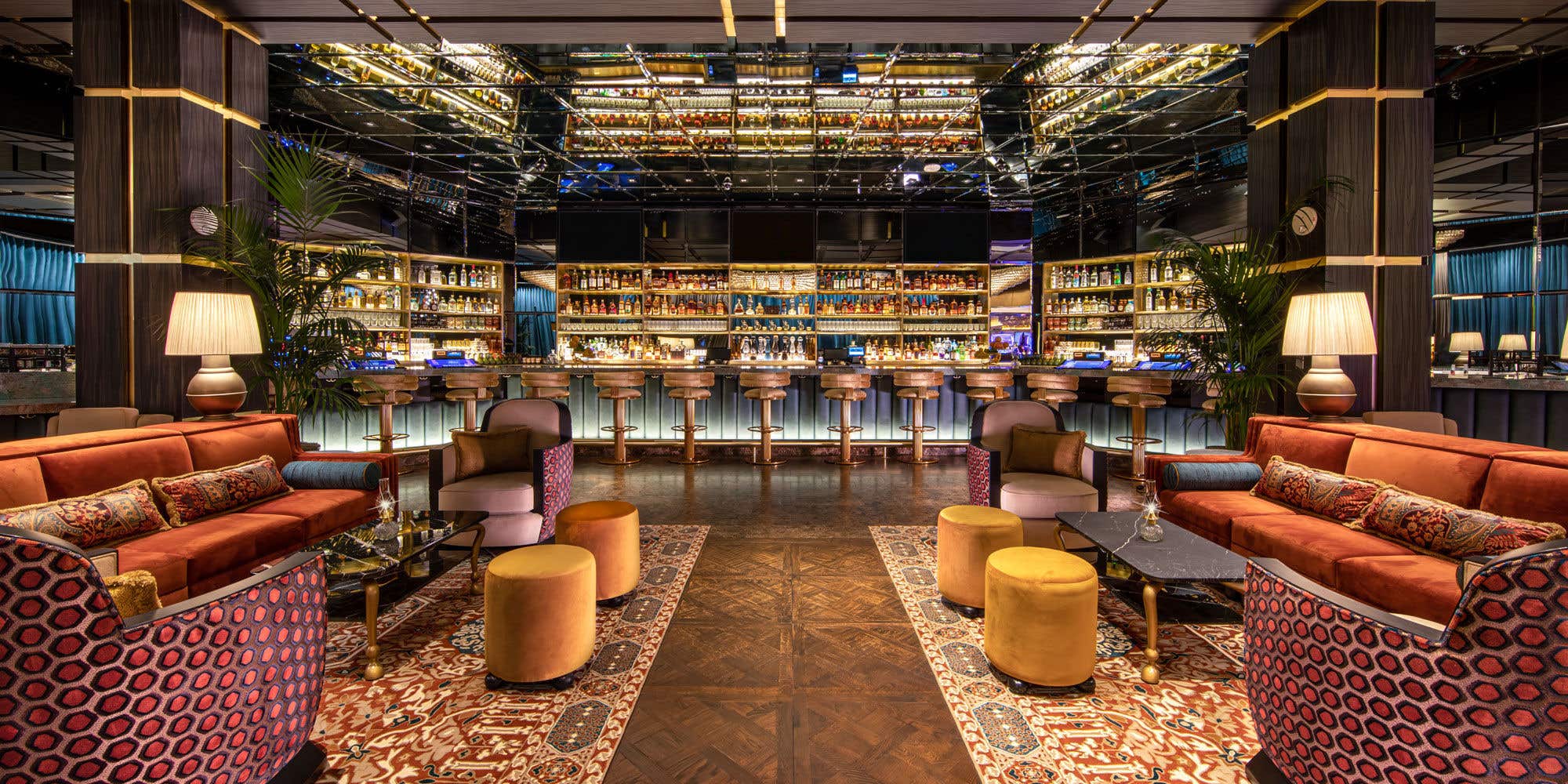 Luxurious bar lounge with plush seating, mirrored ceiling, and a well-stocked bar counter in the background.