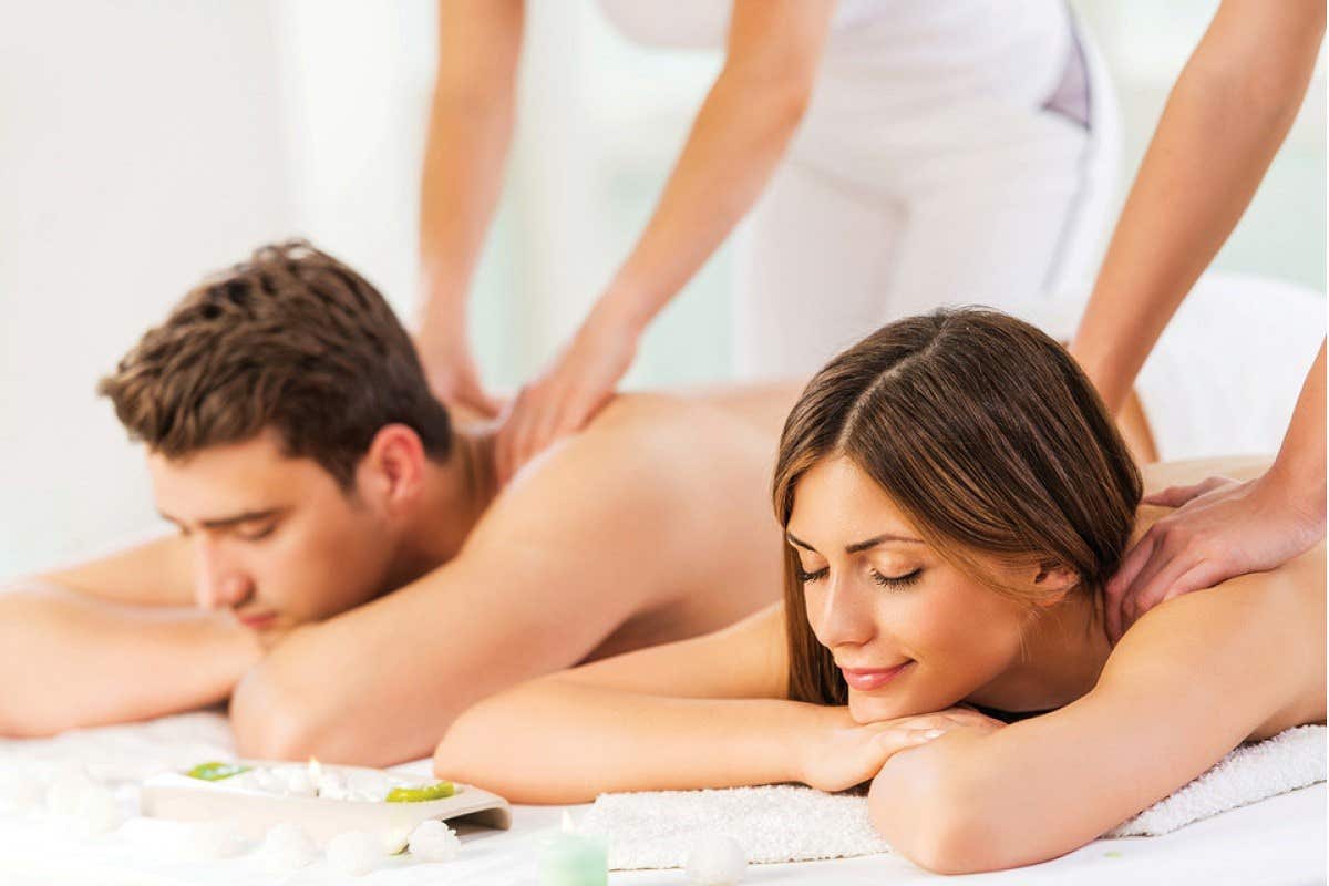 A man and woman lying on massage tables receiving back massages in a serene spa setting.