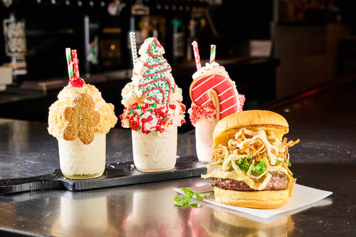 Three festive milkshakes and a burger on a countertop.