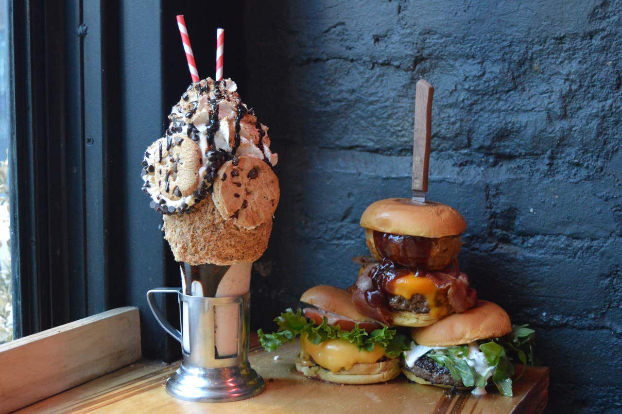 A milkshake with cookies and cream next to a double cheeseburger with bacon and lettuce, served on a wooden board.