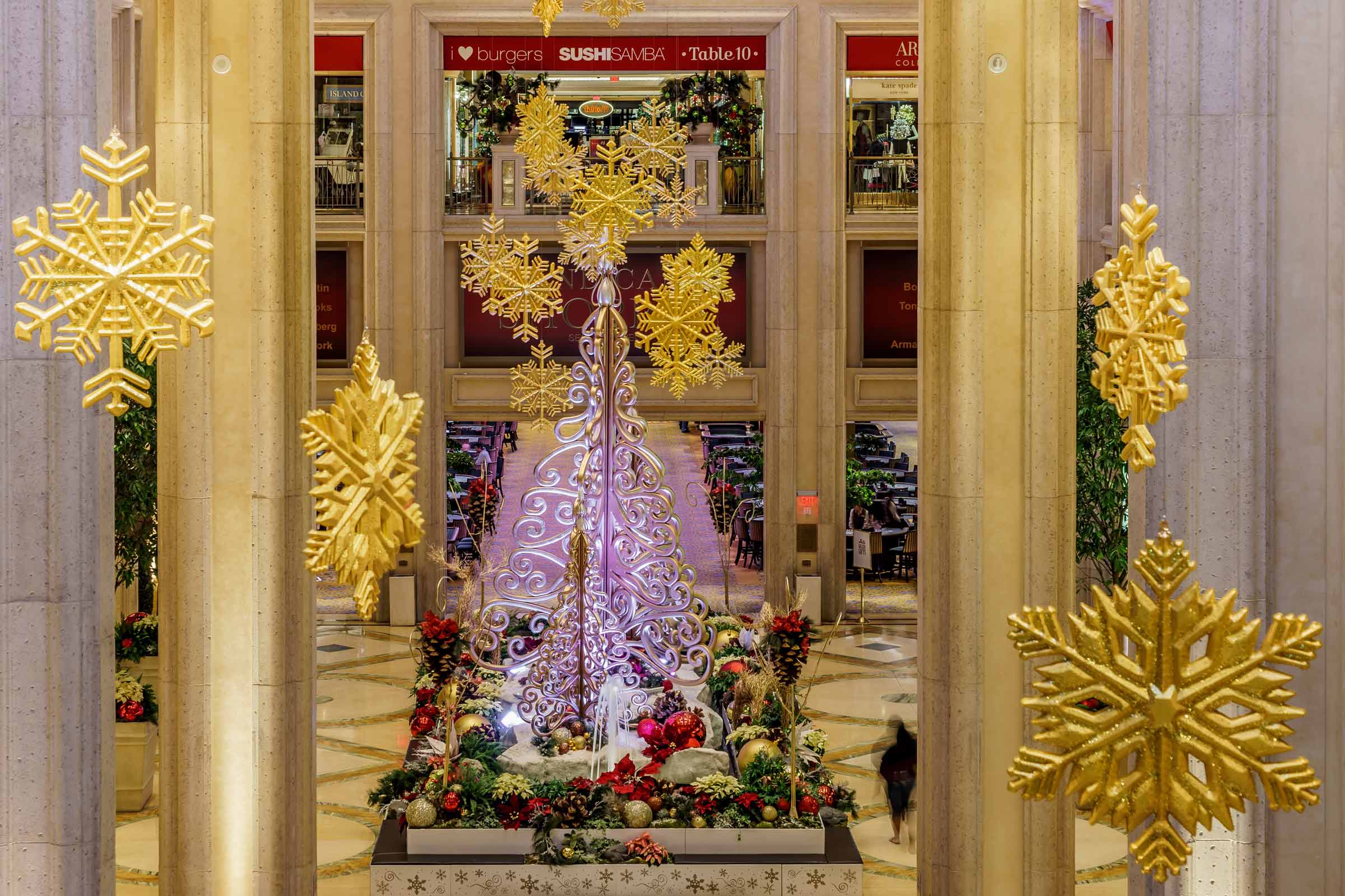 Grand holiday atrium display features a large gold snowflake tree, surrounded by giant golden snowflakes and festive decor.