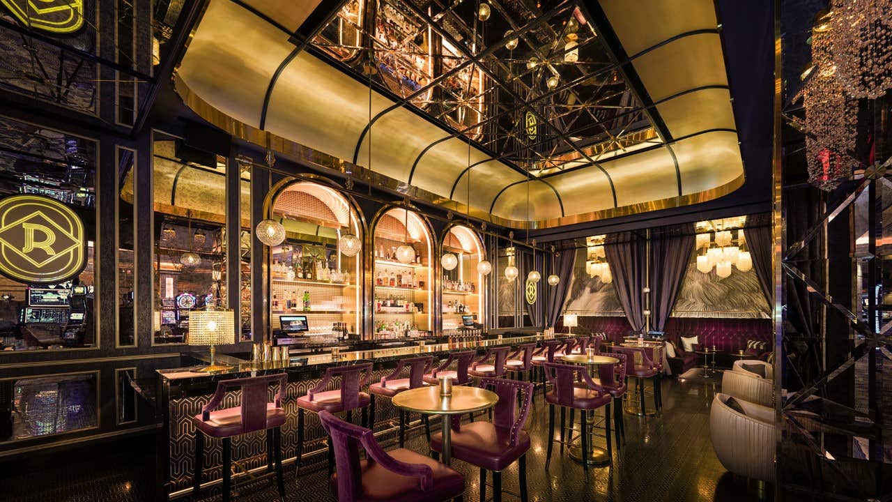 Luxurious bar with purple velvet stools, gold accents, and mirrored ceiling, featuring a well-stocked bar and elegant decor.