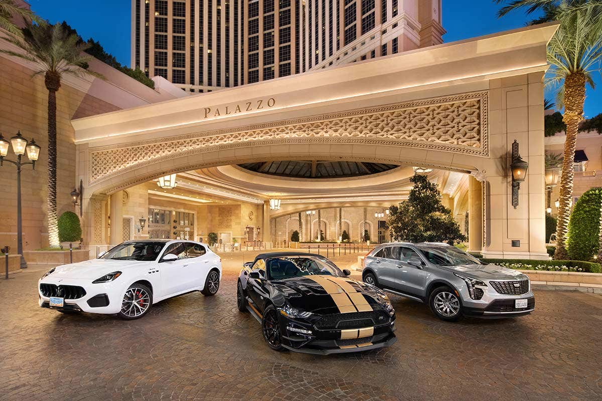 Three luxury cars are parked in front of the Palazzo hotel entrance, including a white SUV, a black sports car, and a silver SUV.