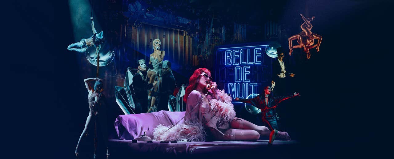 Performers on stage in a theatrical, cabaret-like setting with a "Belle de Nuit" neon sign in the background.