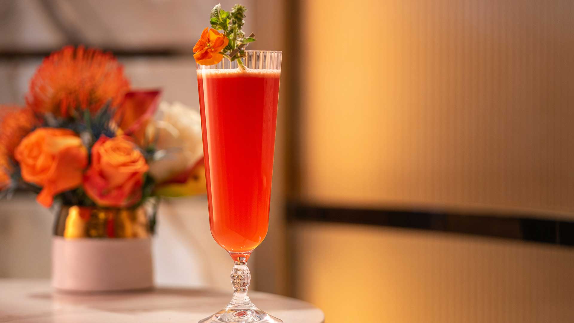 Cocktail in a long glass with a small orange flower for garnish