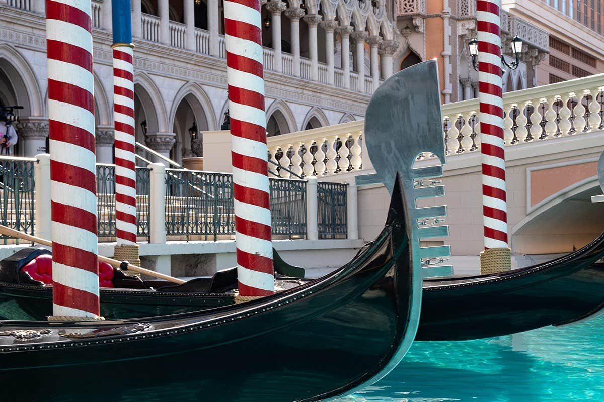 Gondolas moored by the striped poles on a canal, with ornate buildings and arches in the background.