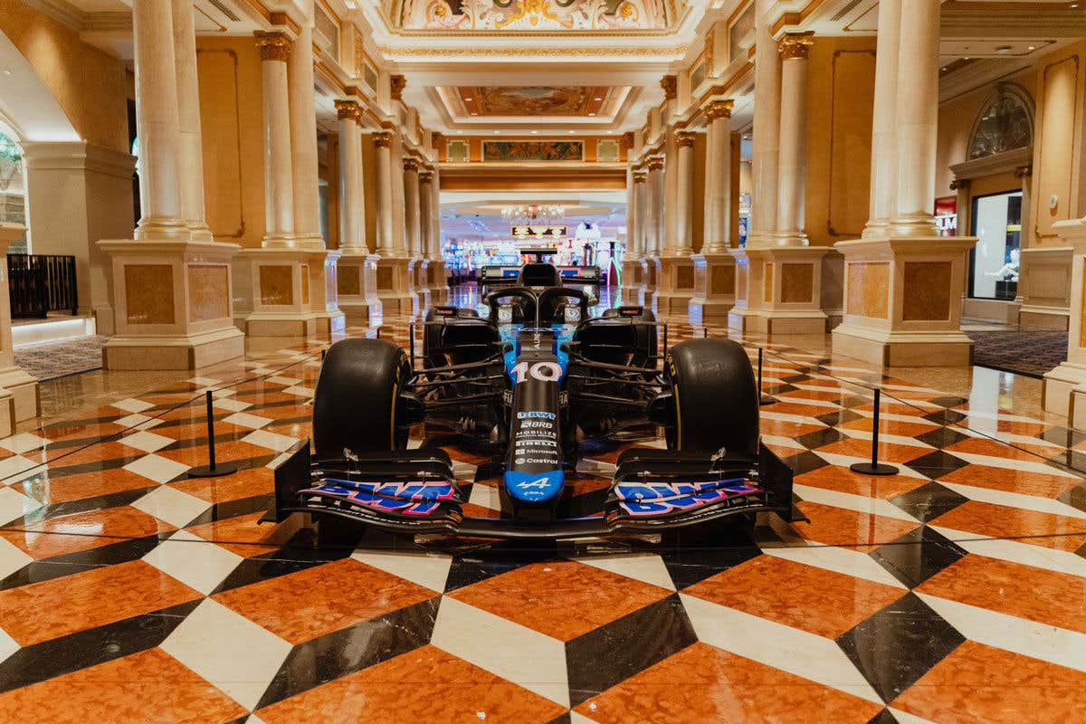 Formula 1 car displayed in an ornate hallway with patterned floor and tall columns.