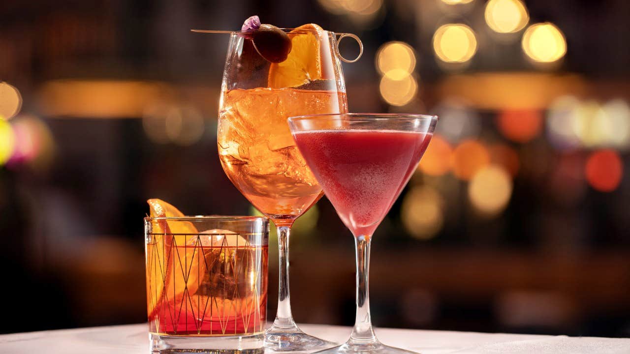 Three vibrant cocktails in elegant glasses on a bar counter with warm, bokeh lighting in the background.