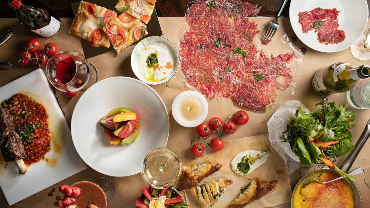 An overhead view of a table filled with various Italian dishes, including meats, cheeses, salad, wine, and other appetizers.