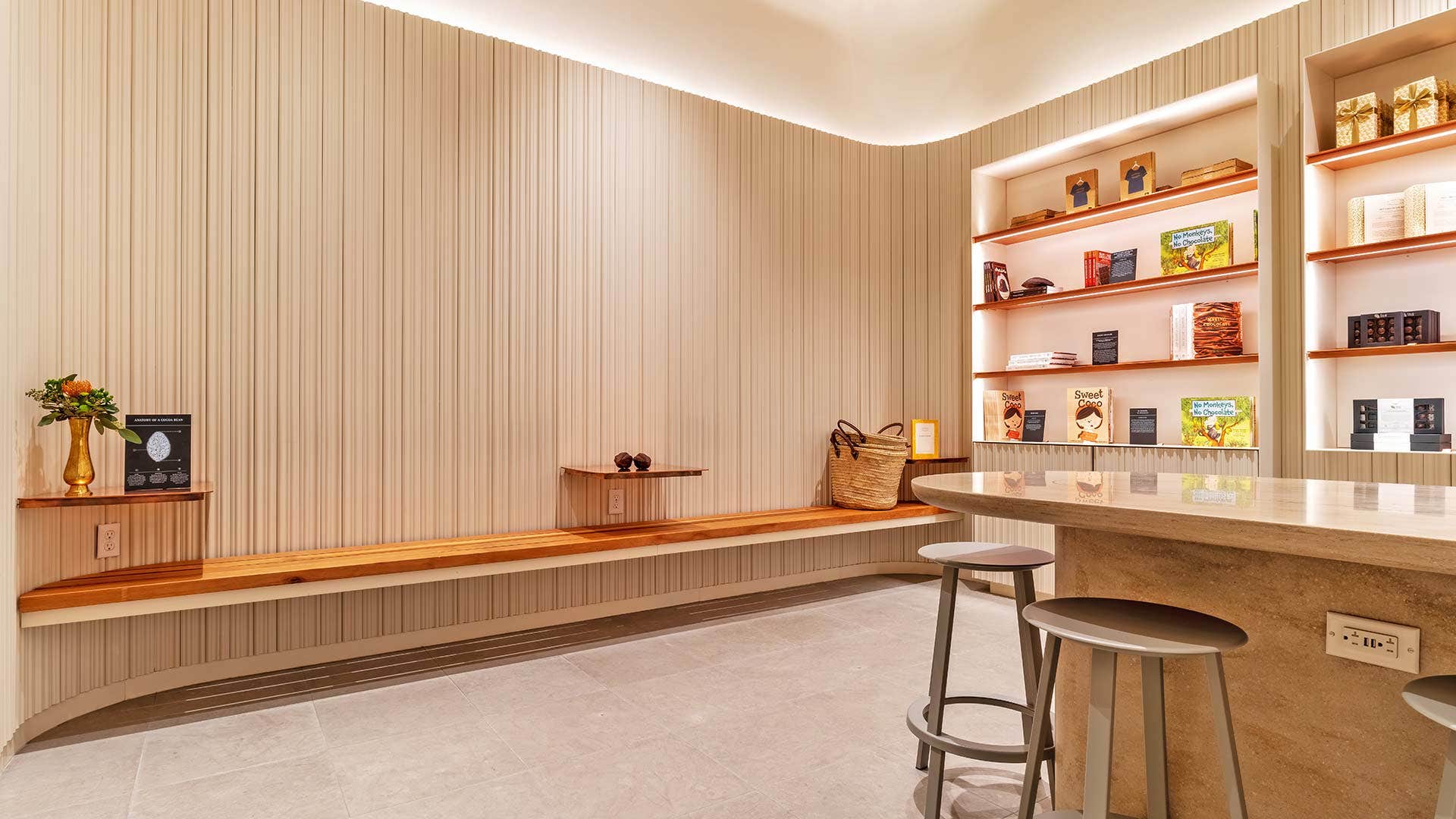 Minimalist cafe with wooden bench seating, a concrete counter, modern shelves displaying items, and a basket in the corner.