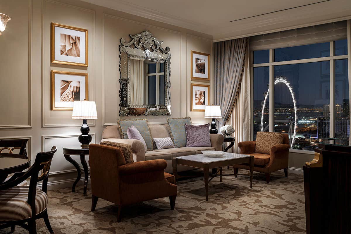 Elegant hotel room with a sofa, two armchairs, a coffee table, and a large window overlooking a Ferris wheel at night.