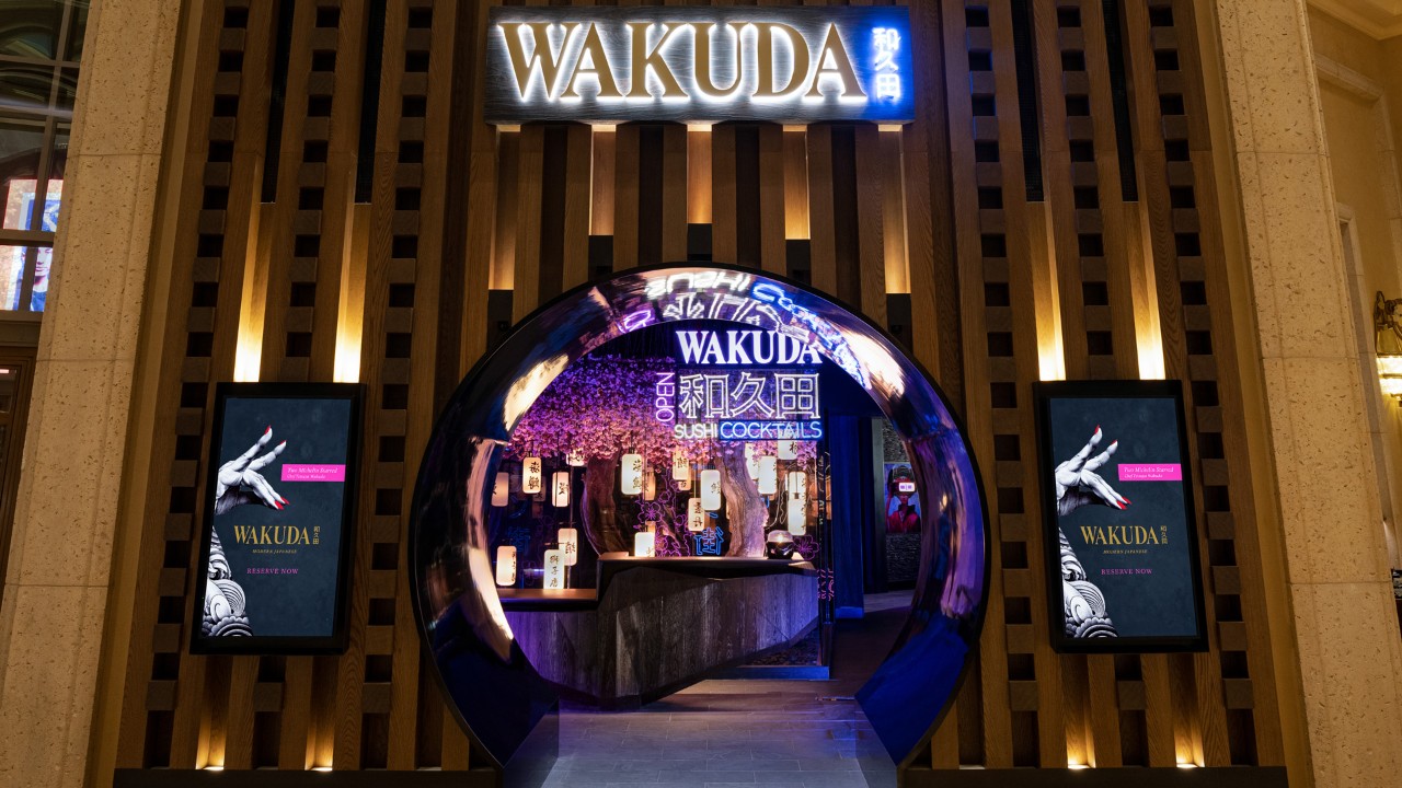 Entrance of Wakuda restaurant with a circular entrance, purple lighting, and digital menu screens on both sides.