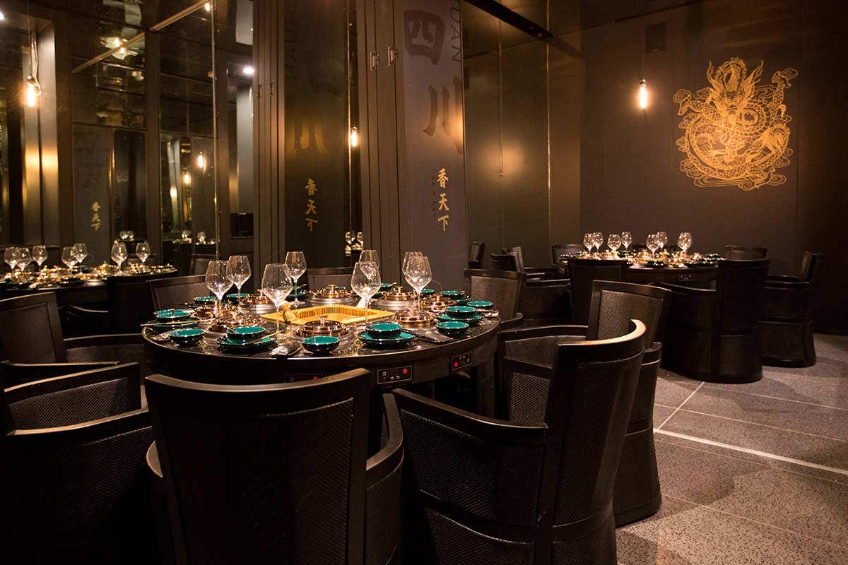 Elegant restaurant dining area with round tables, set with glassware and plates, dim lighting, and ornate wall art.