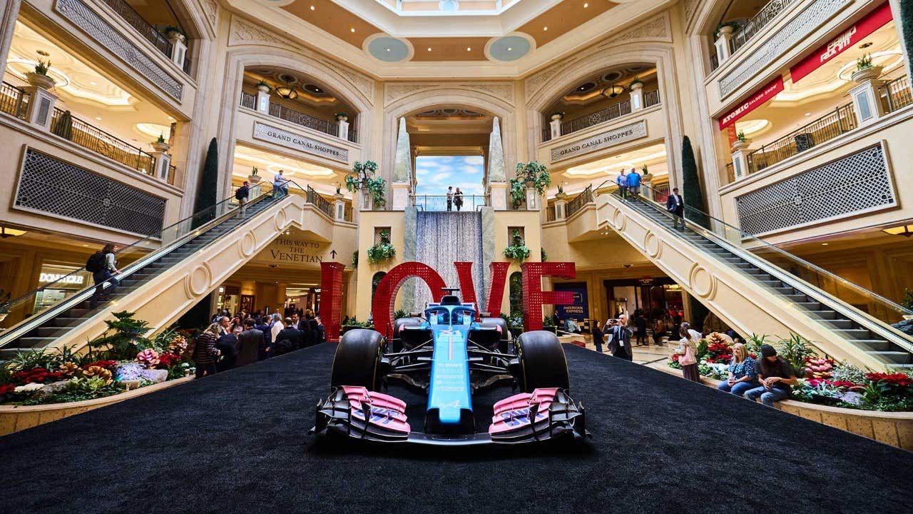 A Formula 1 race car displayed in a grand mall with large 'LOVE' letters and people on stairs and balconies around.