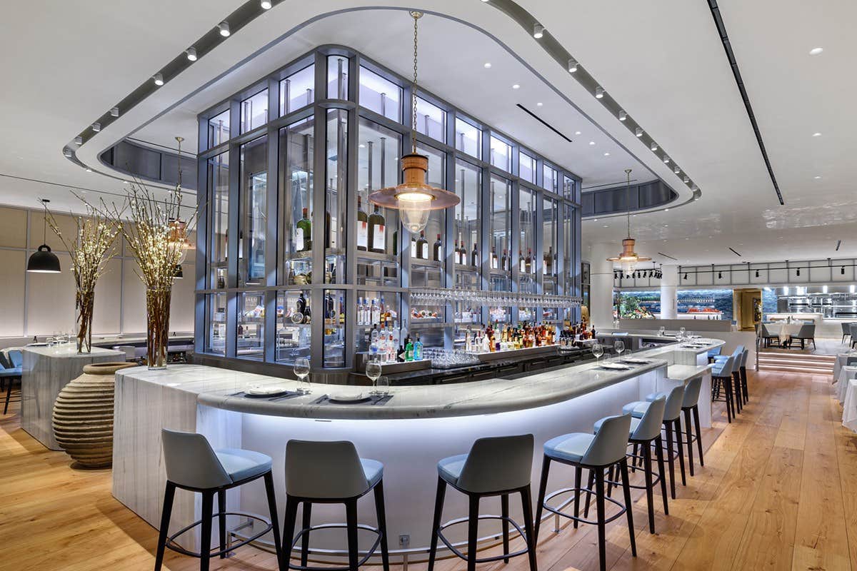 A modern, stylish bar with a circular counter, high chairs, and a central glass display of bottles and lights.